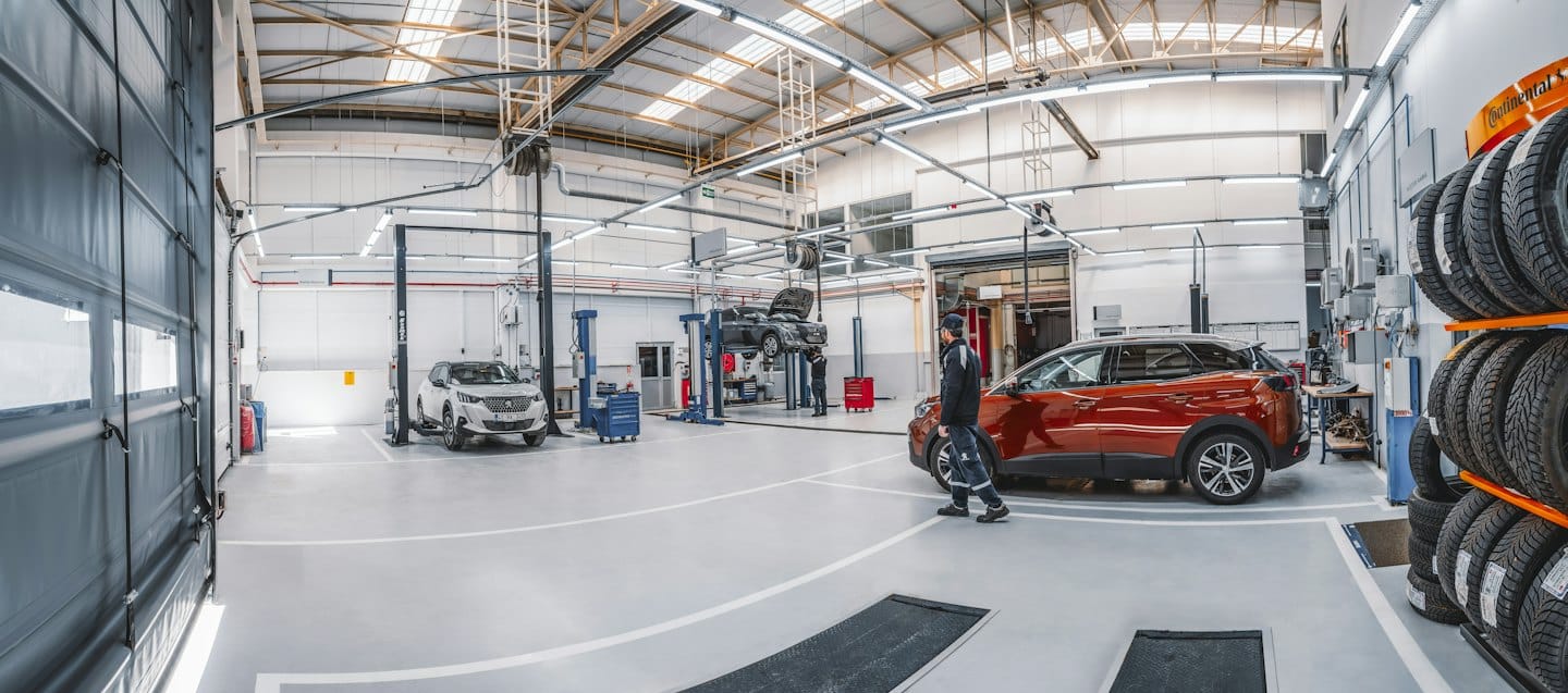 Technician walks towards orange SUV in a bright auto repair shop.
